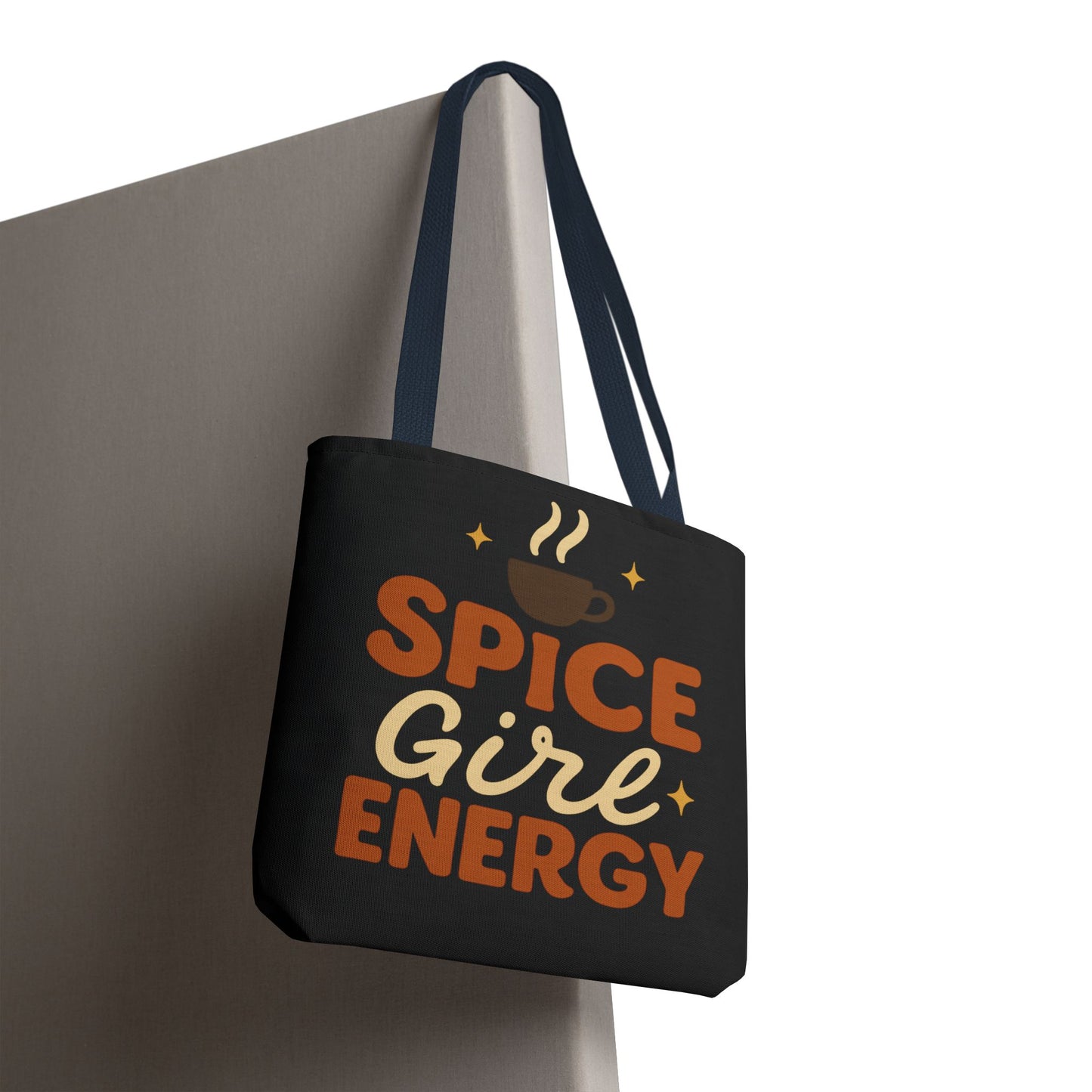 “Spice Girl Energy” tote bag in black with navy handles hanging on wall — modern fall tote for coffee lovers and gift giving.