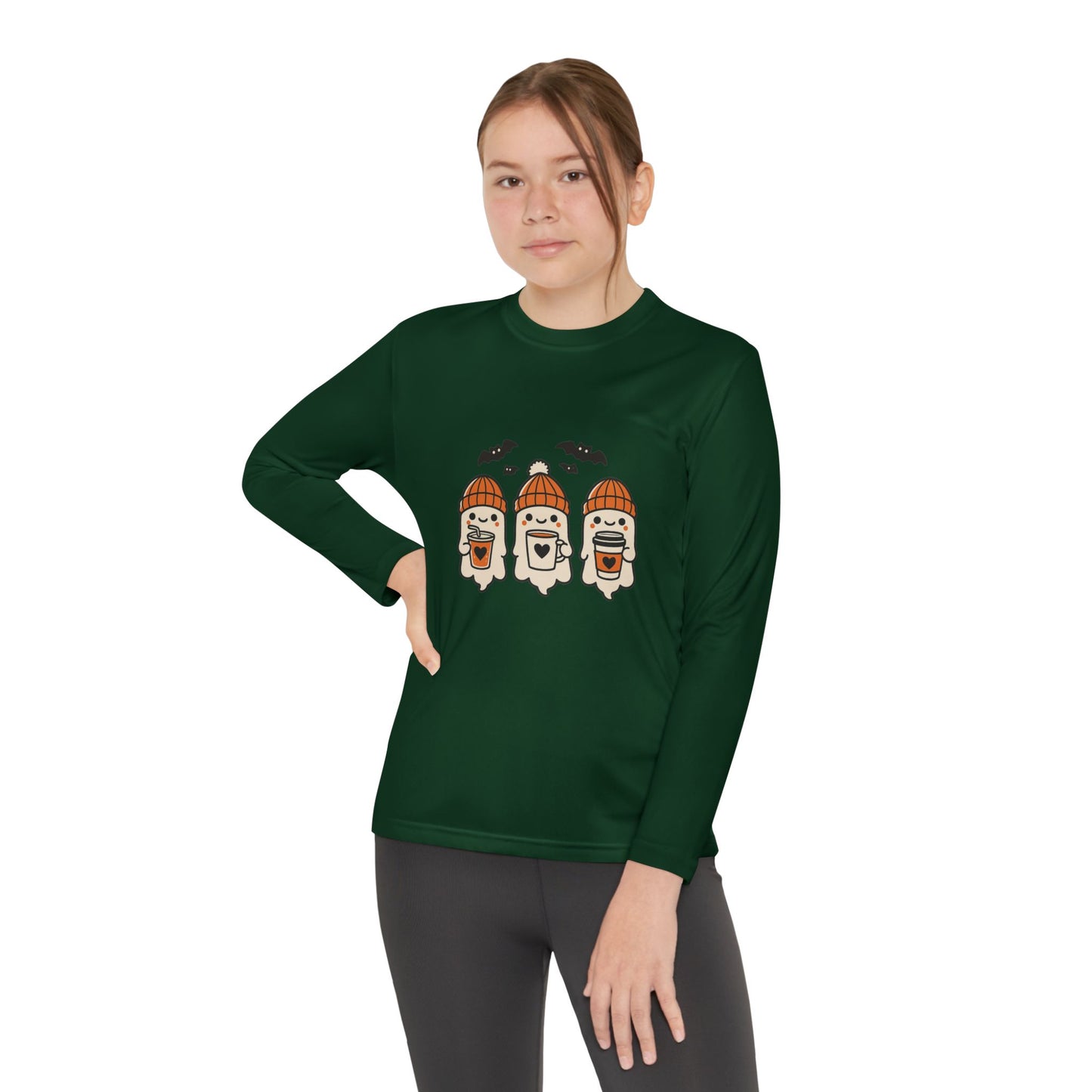young girl wearing dark green long sleeve Halloween shirt featuring three smiling ghosts in orange knit hats holding coffee mugs with bats overhead.