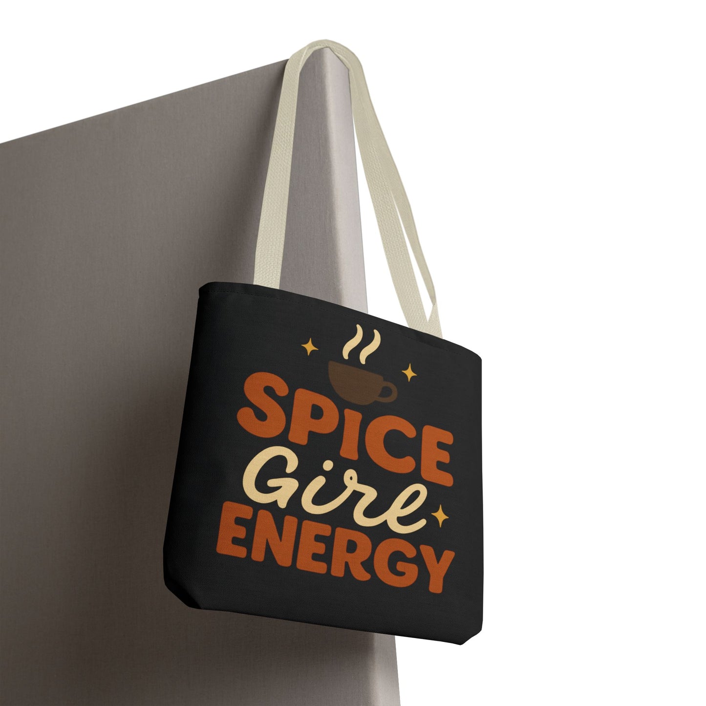 Black “Spice Girl Energy” tote bag with beige straps hanging on wall — autumn coffee tote with retro charm and warm tones.