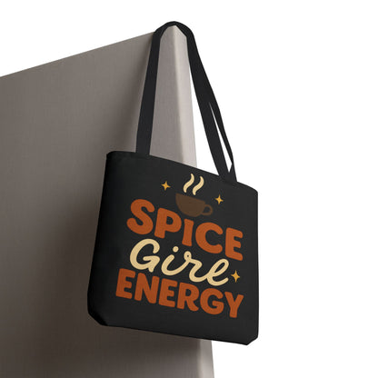 Black “Spice Girl Energy” tote bag with black handles hanging on wall — chic fall tote with warm tones and coffee cup design.
