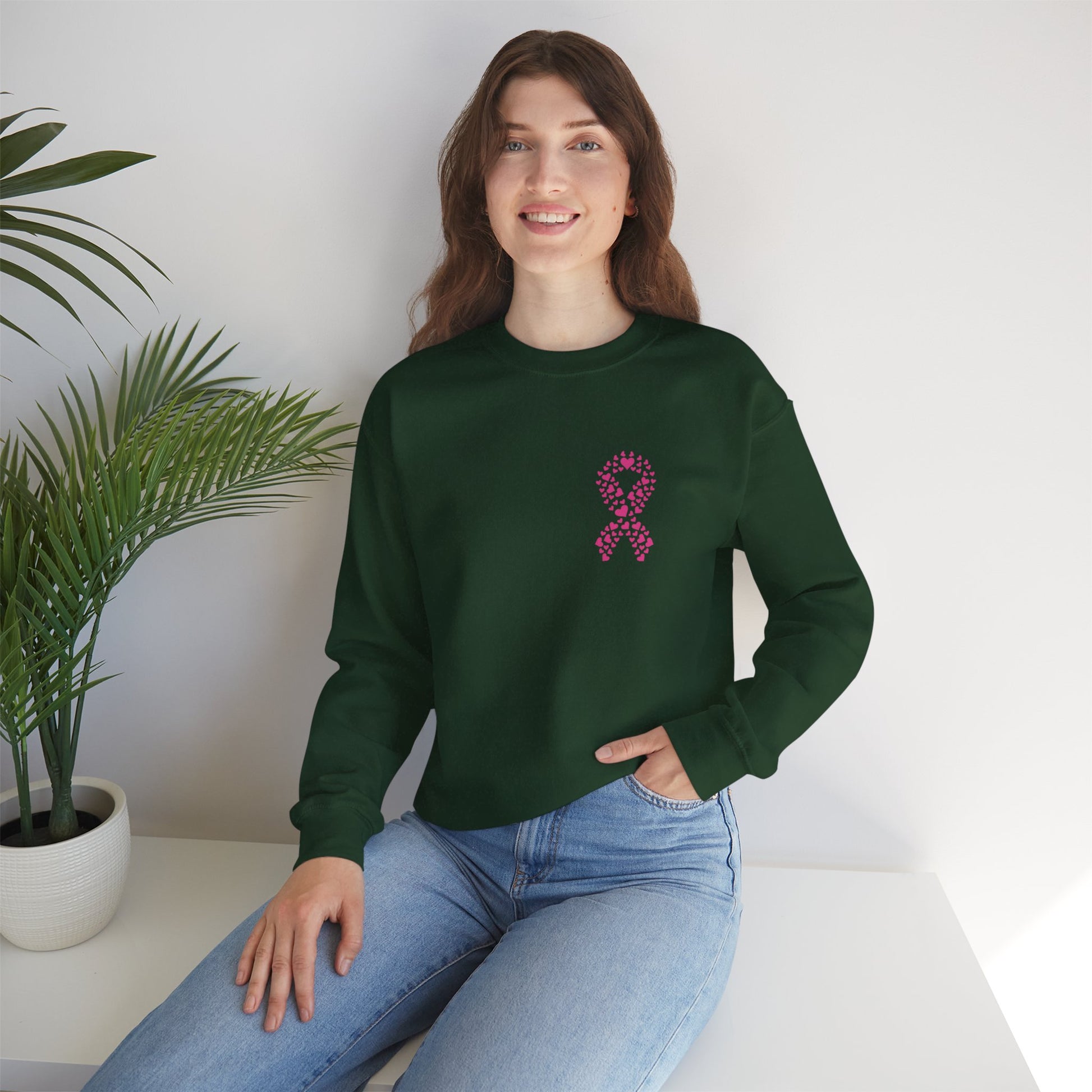 Woman seated wearing forest-green breast cancer awareness crewneck sweatshirt with pink ribbon heart design, Makin’ It by Lady Ev.