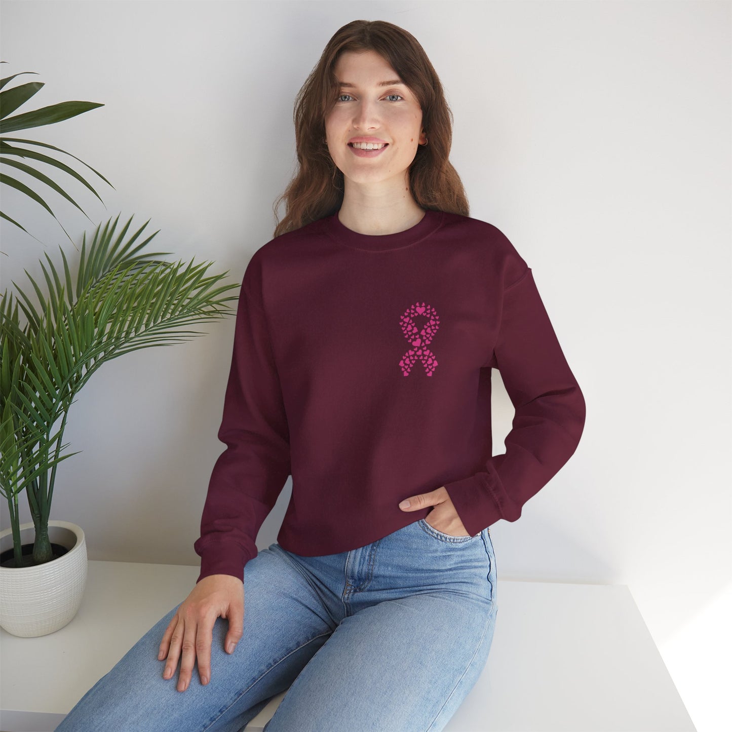 Woman seated wearing maroon breast cancer awareness crewneck sweatshirt displaying pink heart ribbon graphic, Makin’ It by Lady Ev.