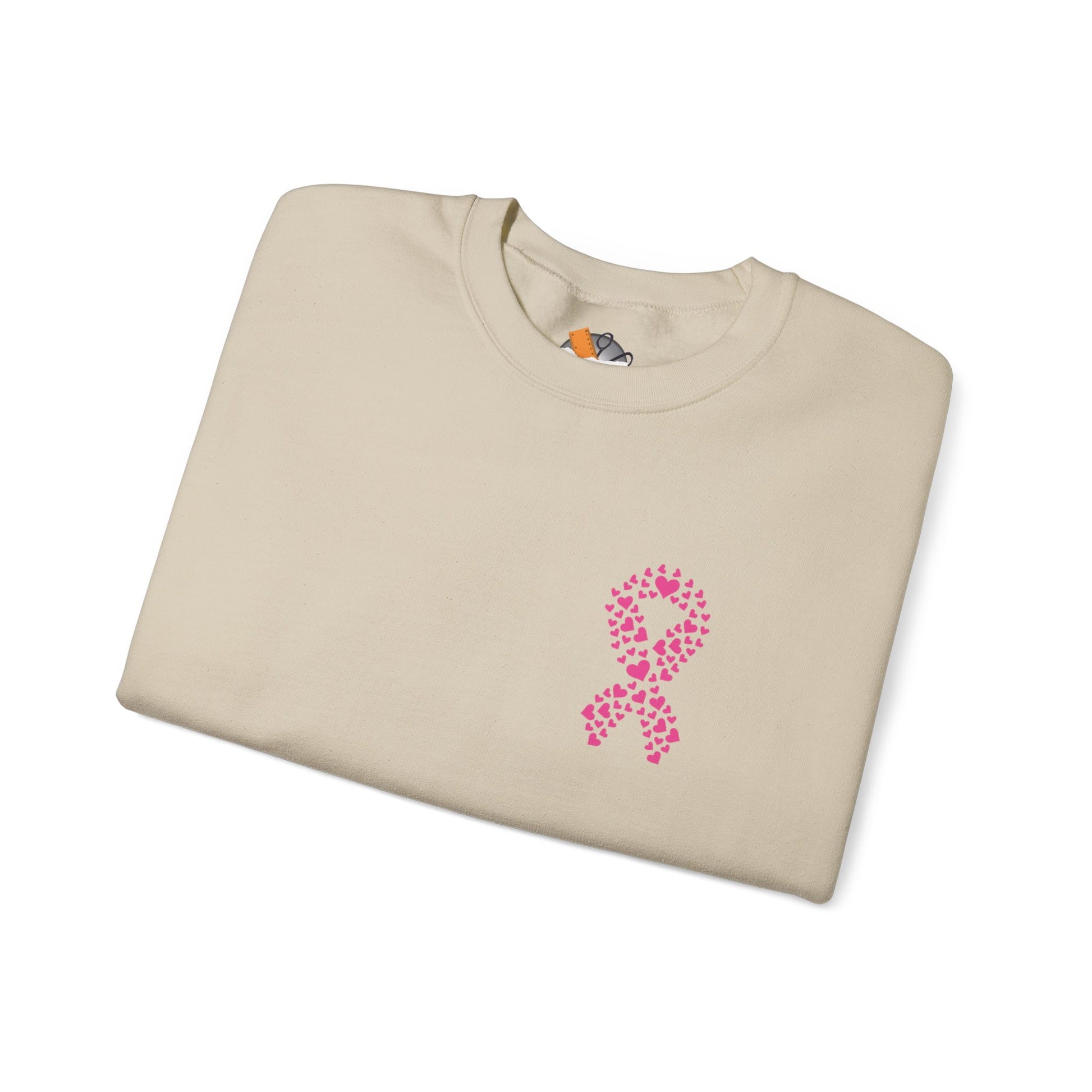 Folded sand crewneck sweatshirt featuring pink heart-shaped ribbon design for breast cancer awareness, Makin’ It by Lady Ev.