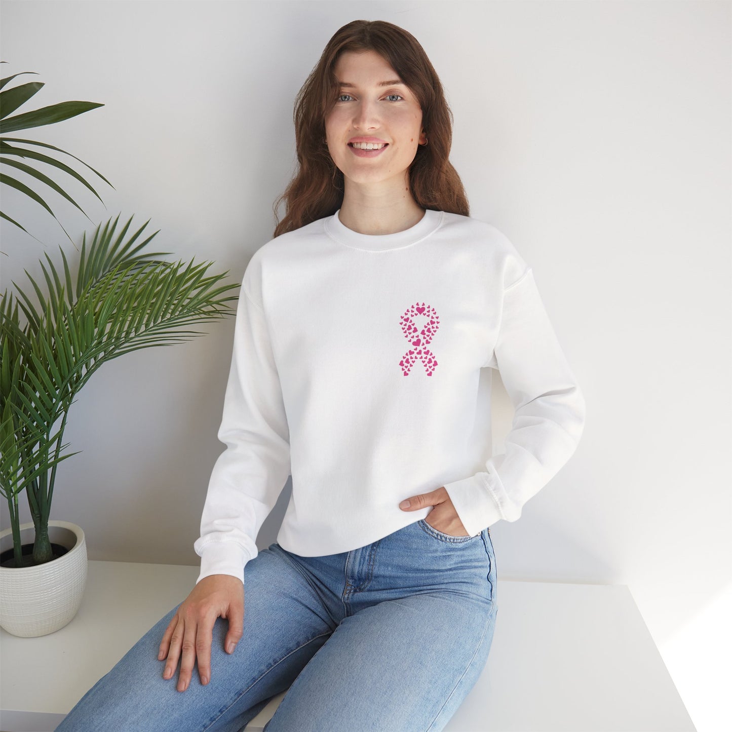 Woman seated in white breast cancer awareness crewneck sweatshirt featuring pink ribbon heart graphic, Makin’ It by Lady Ev.