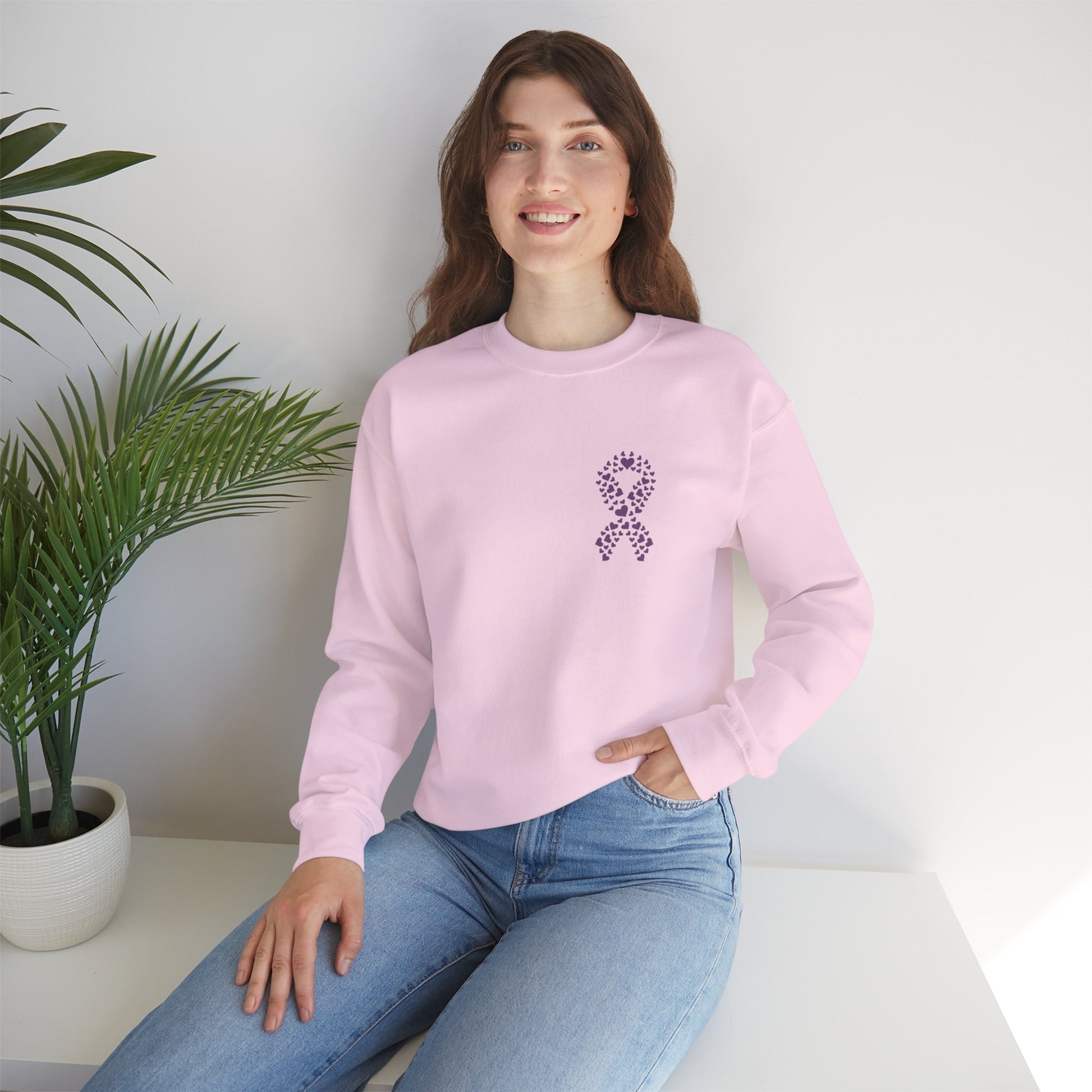 Woman seated in pink domestic violence awareness crewneck sweatshirt with purple heart ribbon graphic, Makin’ It by Lady Ev.