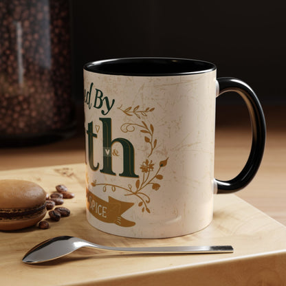 Lifestyle image of black “Fueled by Faith & Pumpkin Spice” 11oz accent mug — Christian fall mug on wooden table beside macaron and coffee spoon.