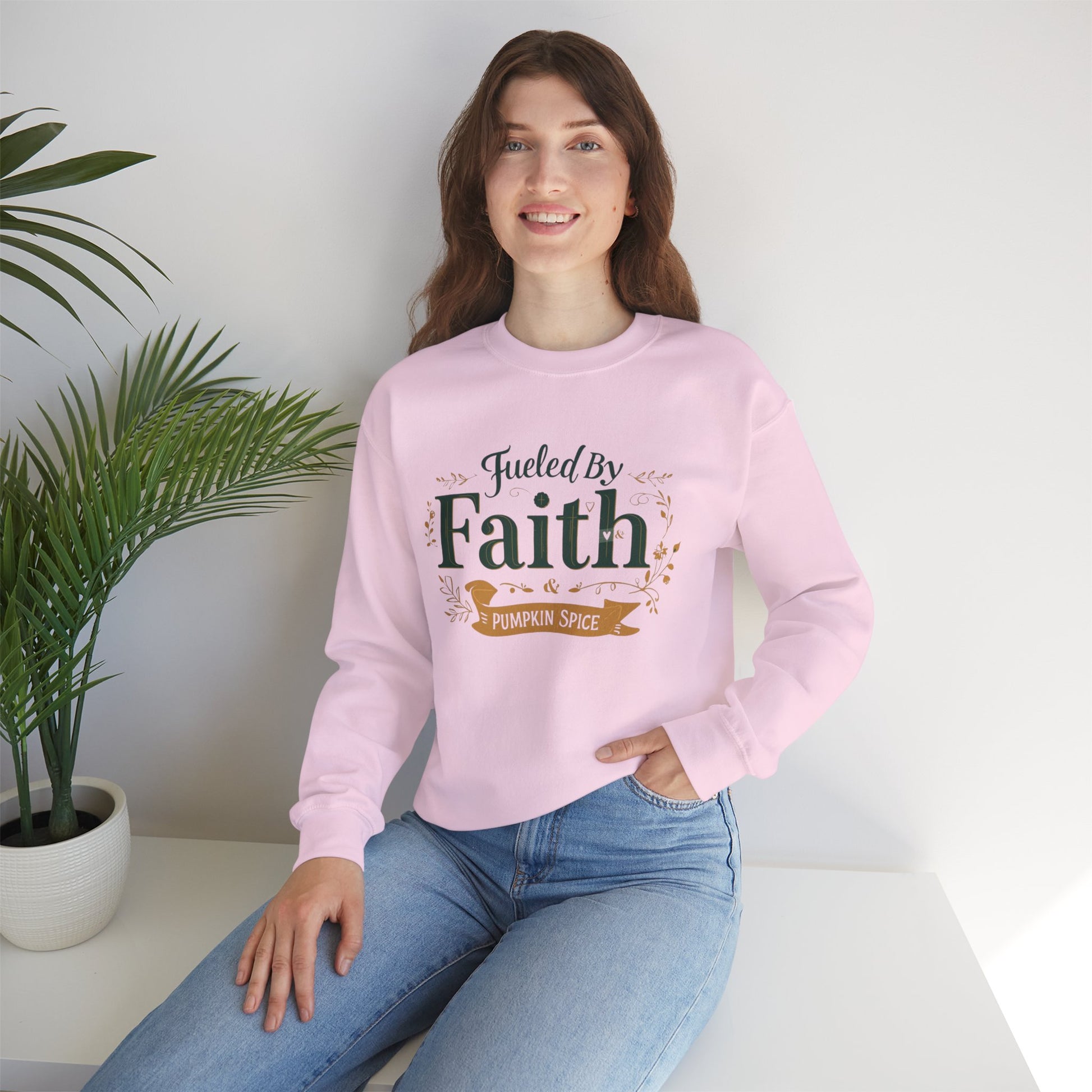 Woman sitting near window in light pink “Fueled by Faith & Pumpkin Spice” crewneck sweatshirt — cozy fall faith-based apparel.