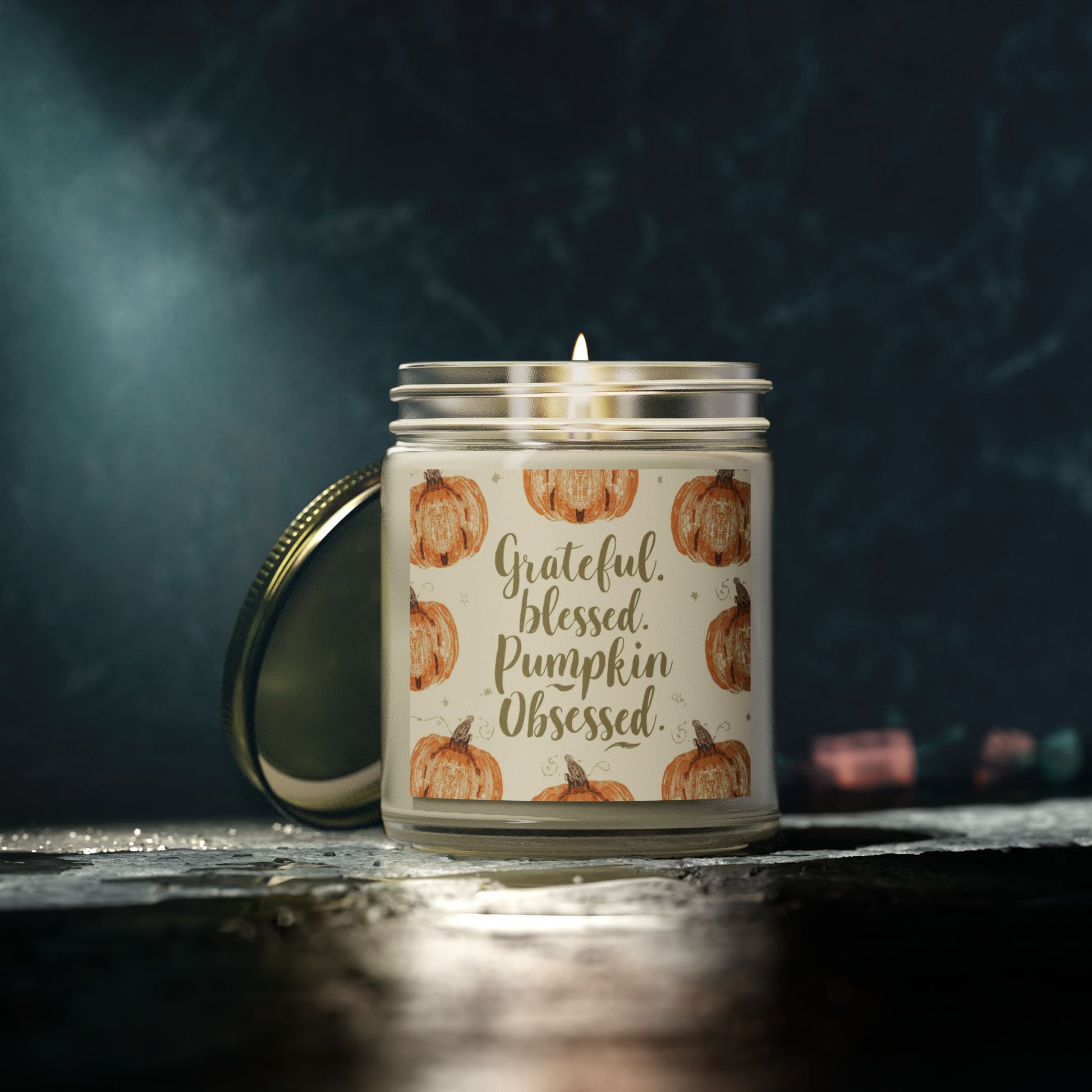 “Grateful, Blessed & Pumpkin Obsessed” clear candle glowing in dark cozy setting — autumn pumpkin candle with warm beachwood scent for home relaxation.
