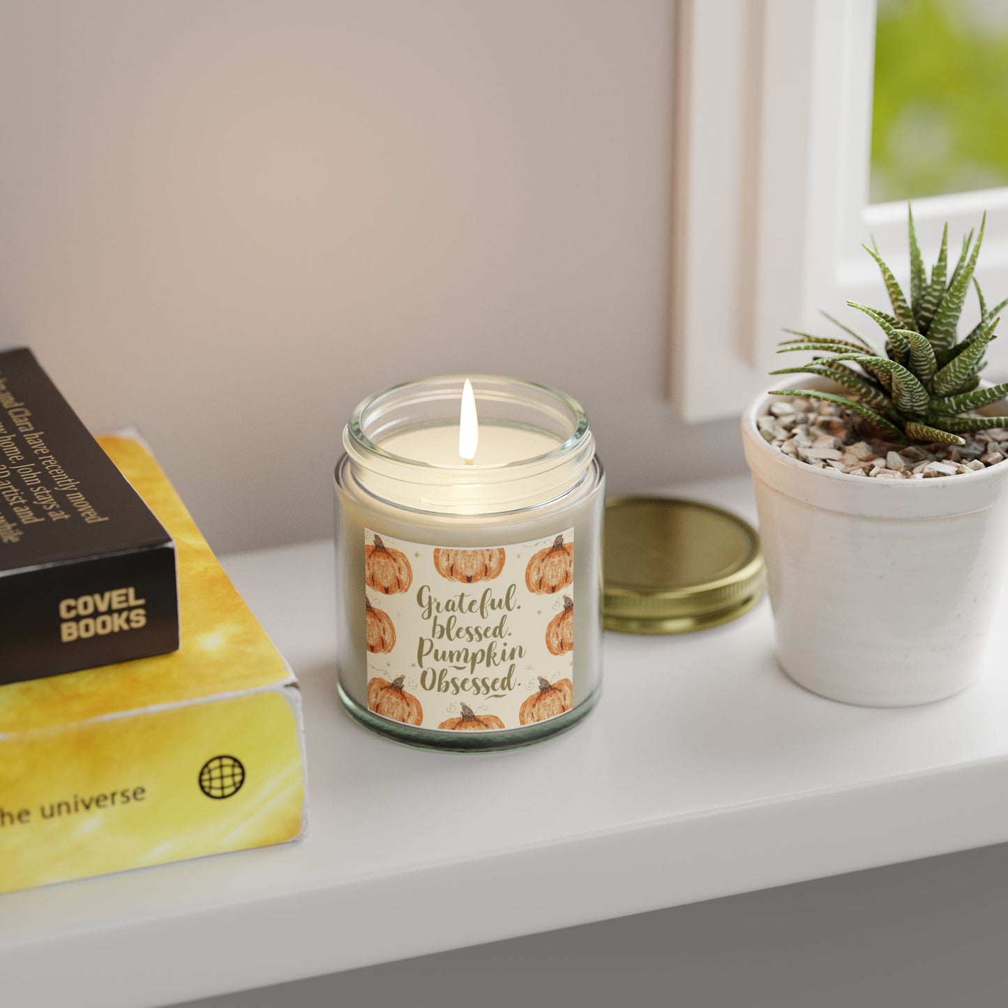 “Grateful, Blessed & Pumpkin Obsessed” clear candle glowing by window — soft blackberry vanilla candle with cozy pumpkin-inspired design.