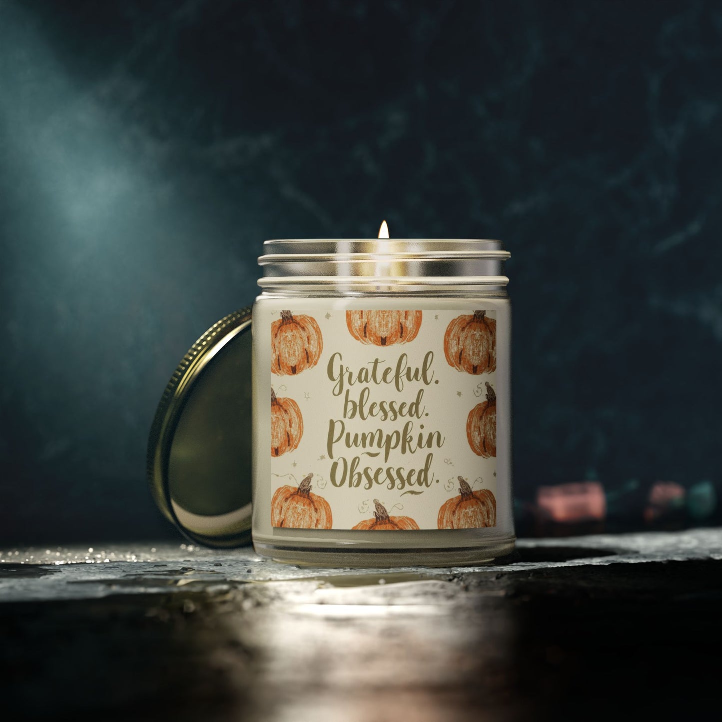 Lit “Grateful, Blessed & Pumpkin Obsessed” clear glass candle in dark ambiance — tropical fall candle with sweet mango coconut fragrance.