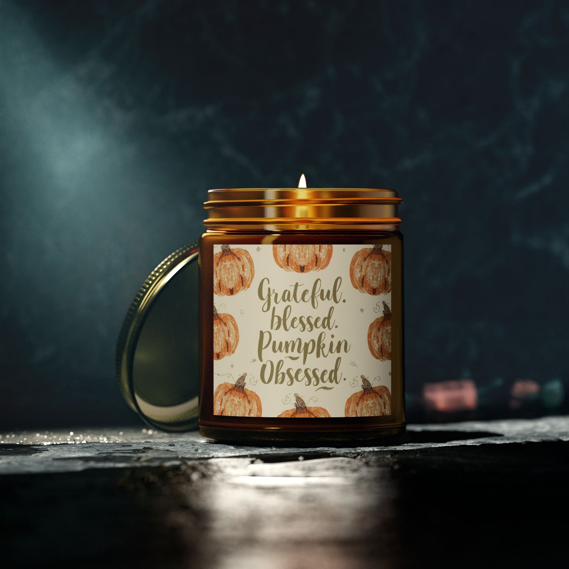 “Grateful, Blessed & Pumpkin Obsessed” amber candle glowing in dark cozy room — elegant unscented pumpkin candle for peaceful ambiance.