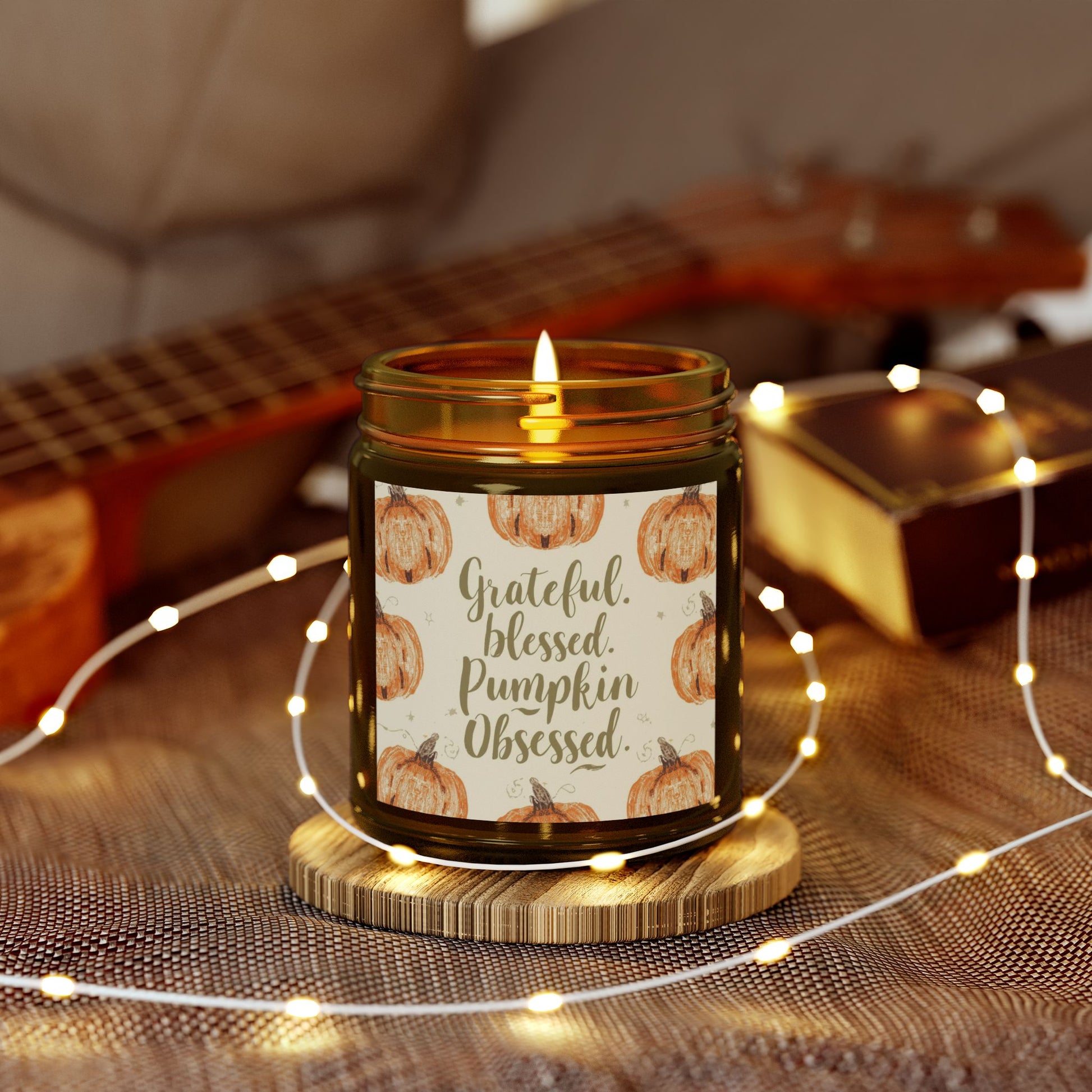 Amber “Grateful, Blessed & Pumpkin Obsessed” candle surrounded by string lights — soft vanilla bean aroma candle ideal for cozy fall nights.