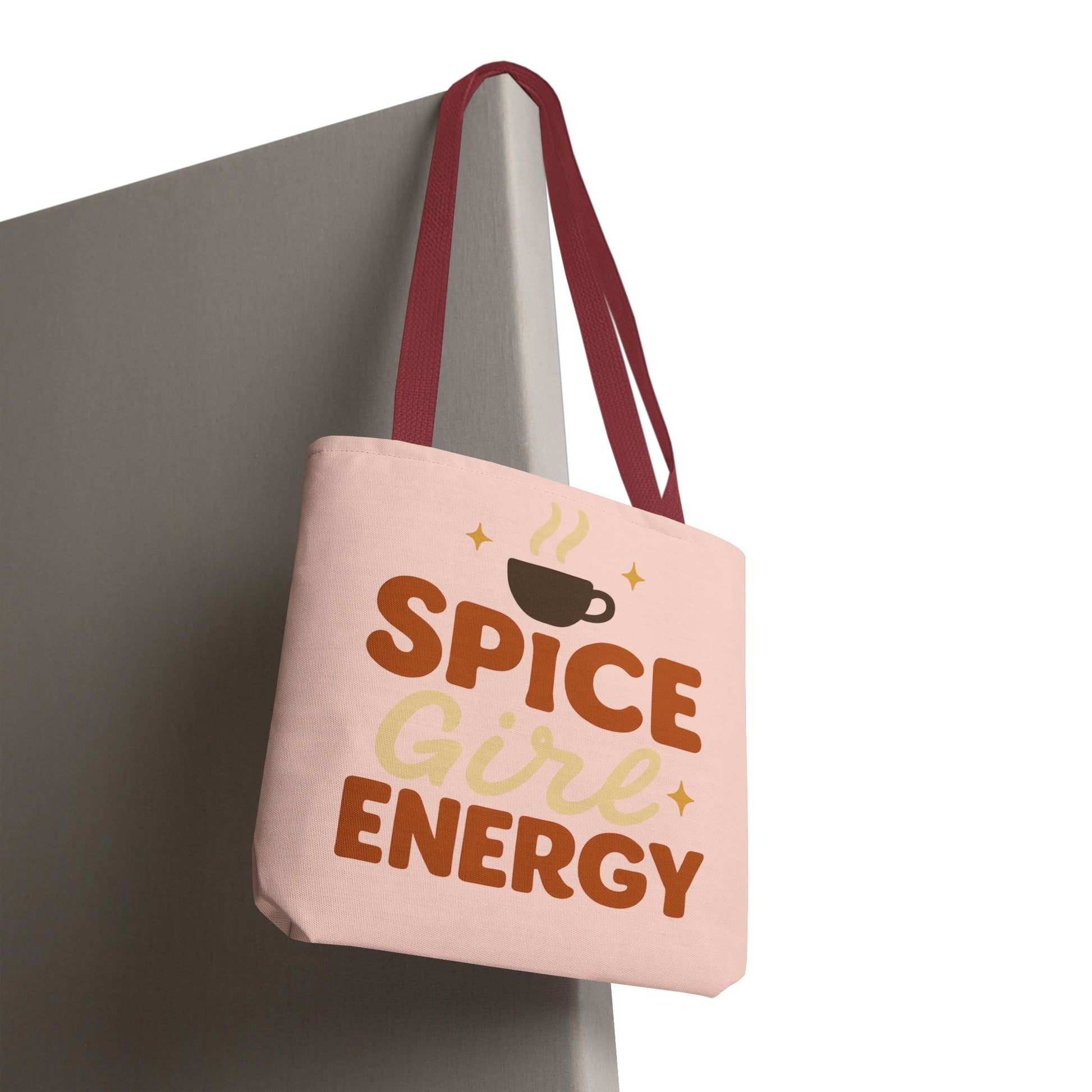 “Spice Girl Energy” tote bag in pale pink with red straps hanging on wall — trendy coffee-themed tote perfect for gifting and daily errands.