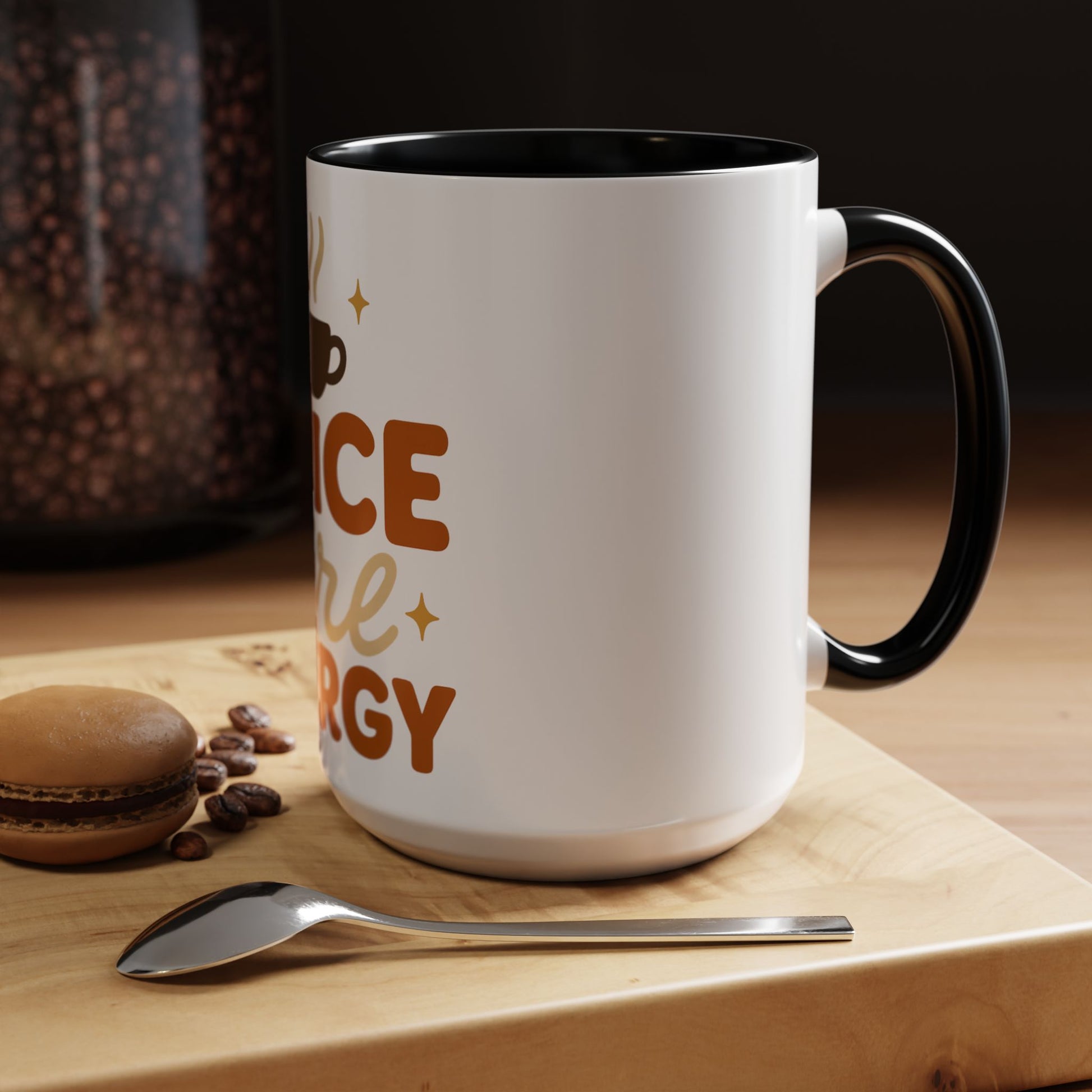 Black “Spice Girl Energy” accent mug on wooden table — white ceramic 15 oz coffee mug with black handle beside spoon and macaron, warm cozy morning scene.