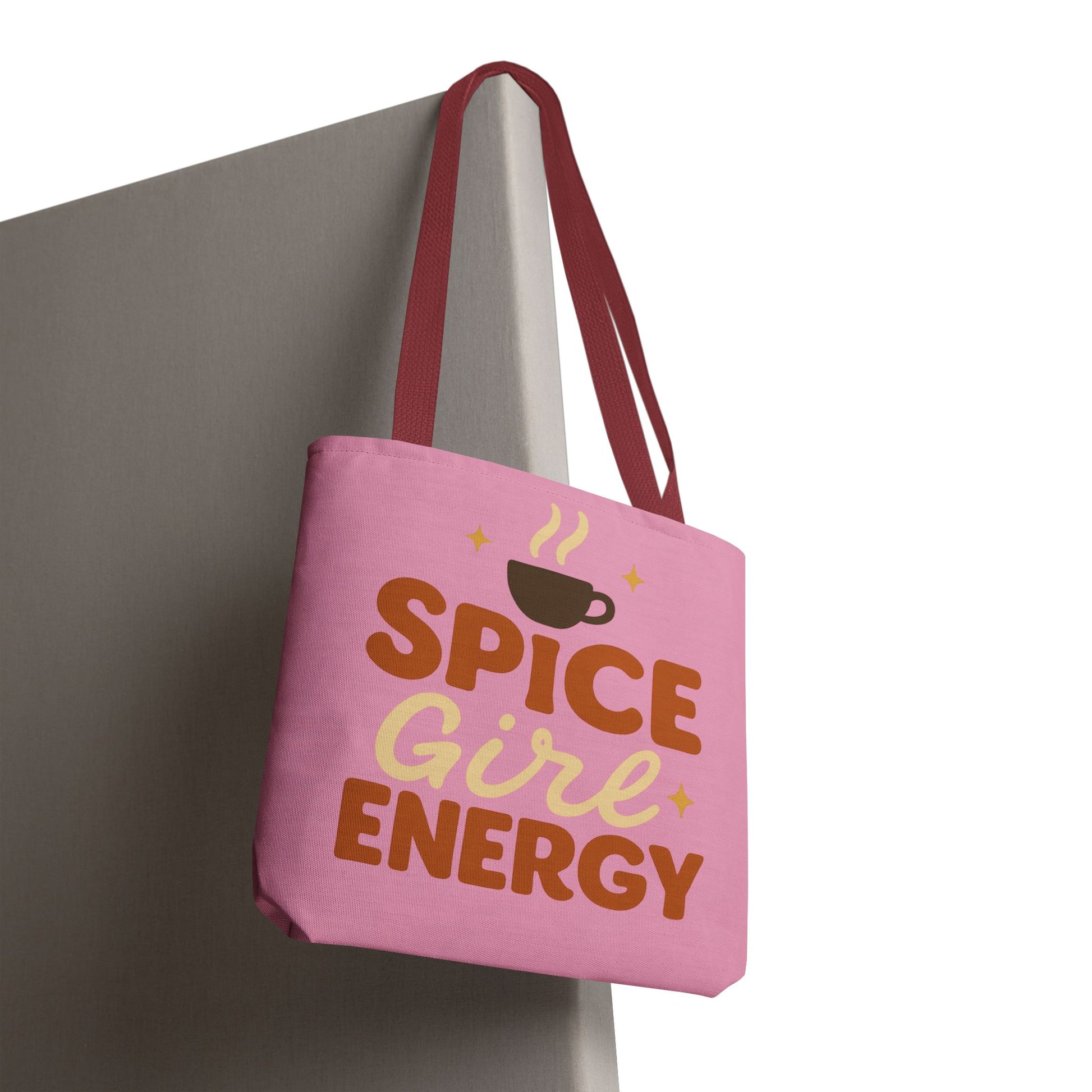 “Spice Girl Energy” tote bag with red straps hanging on wall — stylish pink tote bag for fall season and pumpkin spice lovers.