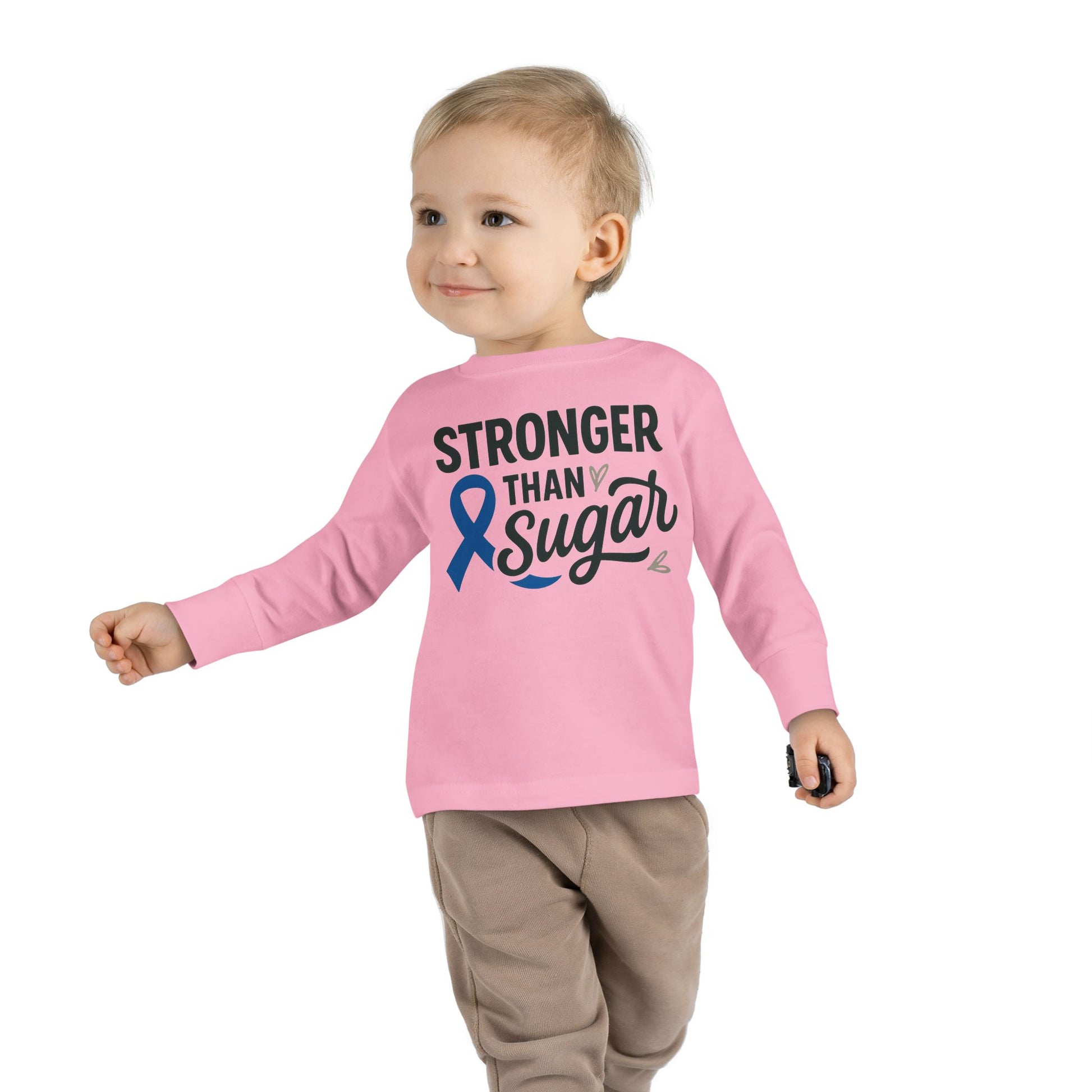 Toddler boy wearing pink Stronger Than Sugar long sleeve shirt — comfortable unisex kids tee featuring blue diabetes ribbon and motivational design.