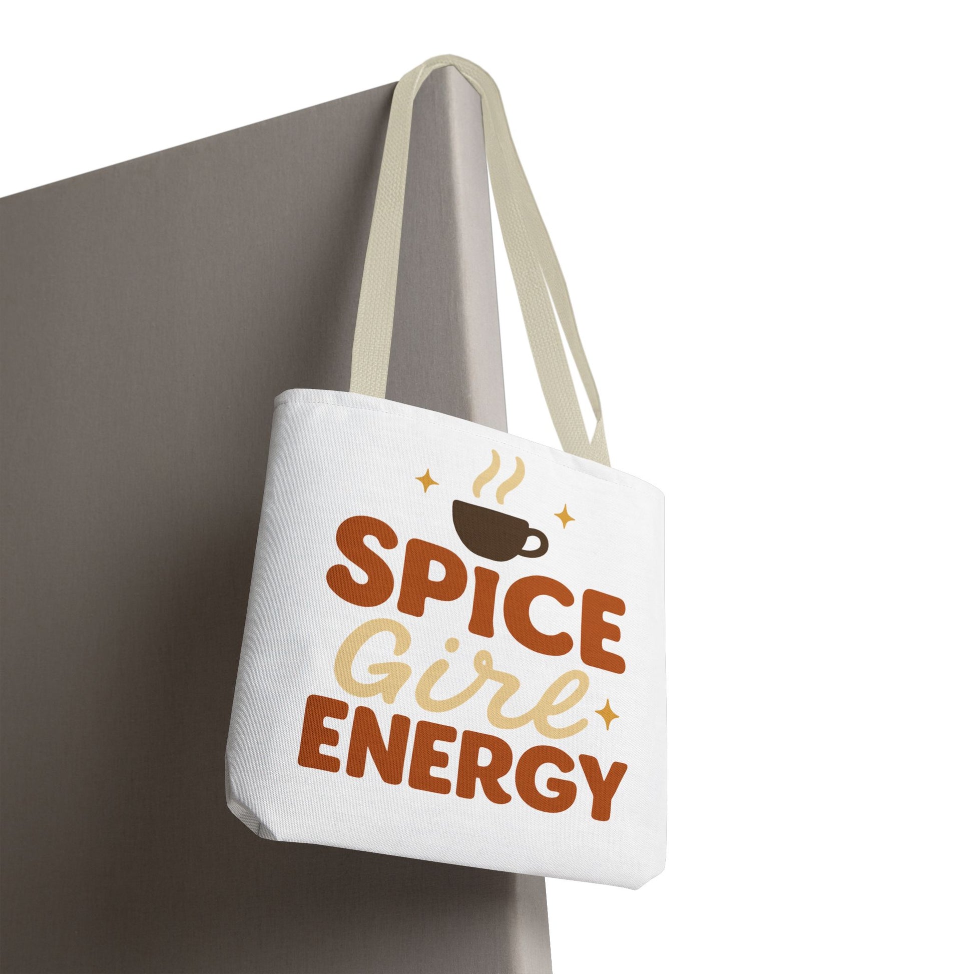 White “Spice Girl Energy” tote bag with beige straps hanging on wall — minimalist autumn tote featuring coffee cup design and retro charm.