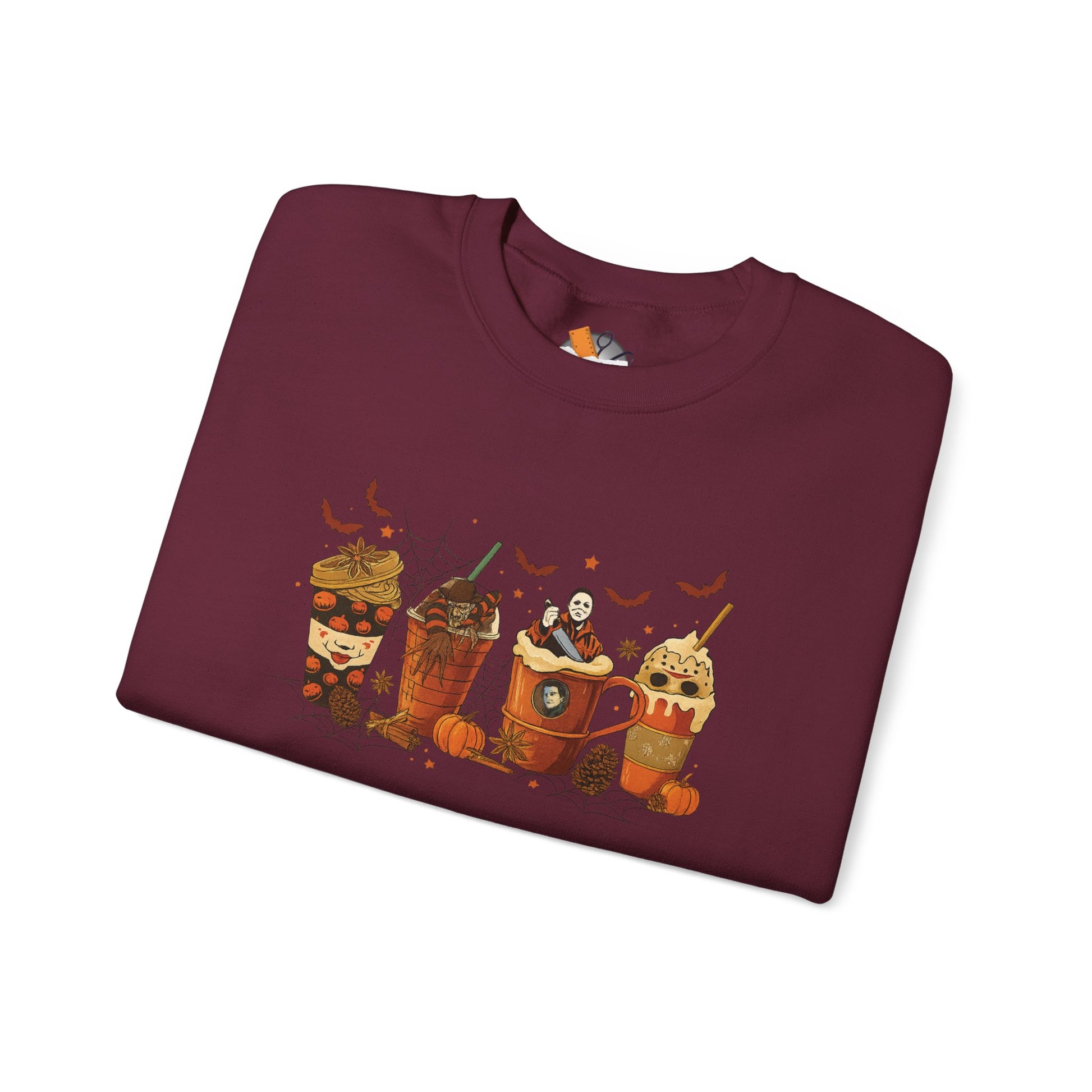 Folded maroon Gildan 18000 crewneck sweatshirt with Halloween horror coffee drinks graphic featuring spooky characters, pumpkins, and bats.